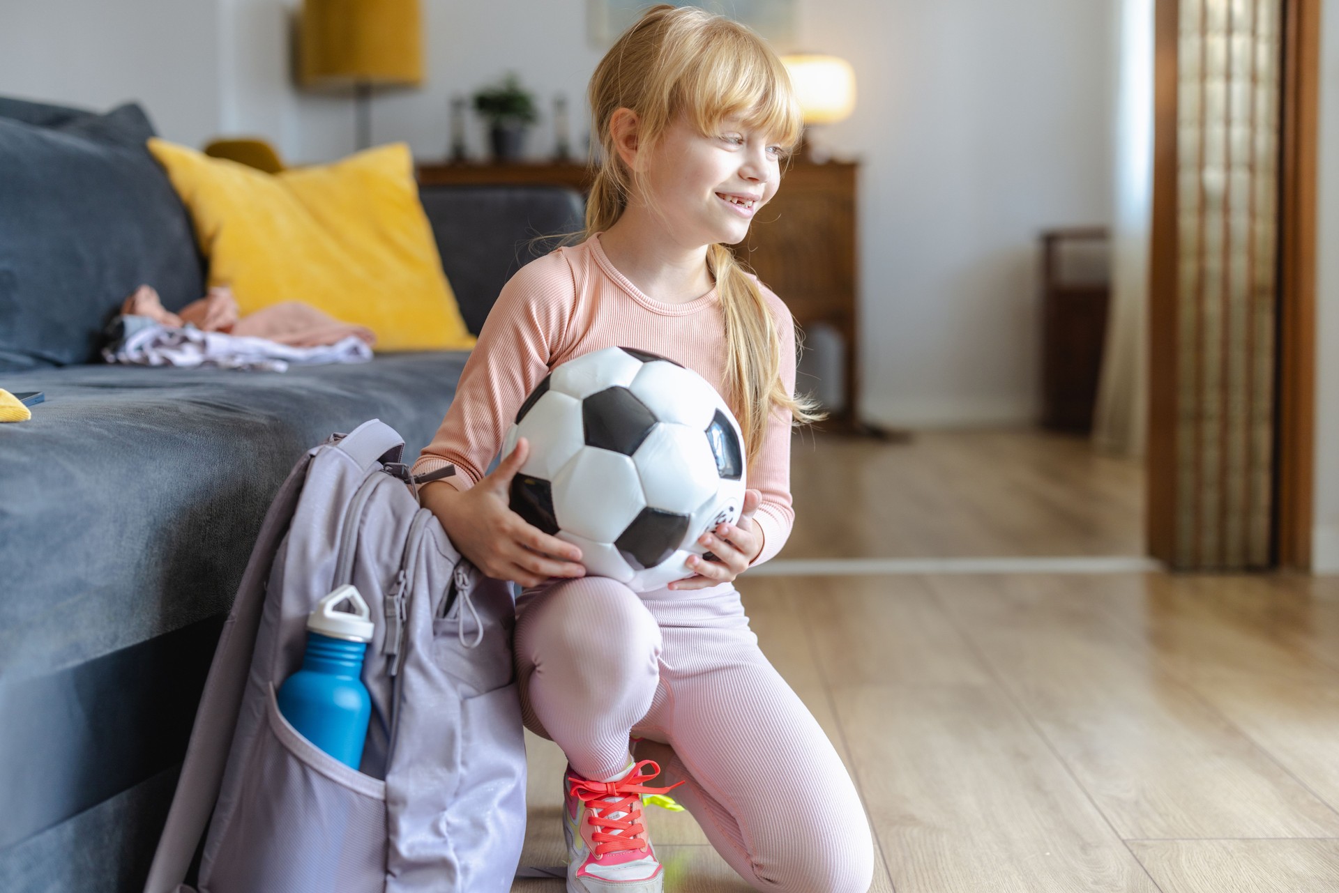 Happy young girl holding soccer ball in living room setting